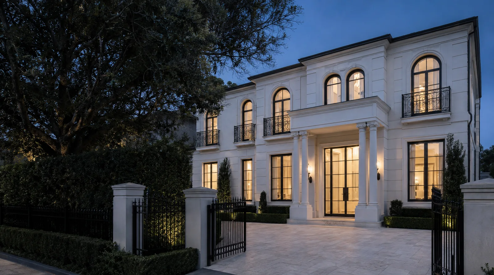 The Holmes Residence at blue hour: white rendered facade, arched windows, portico and iron gates